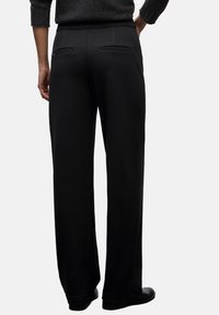 Pantaloni a gamba larga neri realizzati in un tessuto morbido, dotati di due tasche posteriori e un design a vita alta. Frontale piatto e finitura sartoriale.