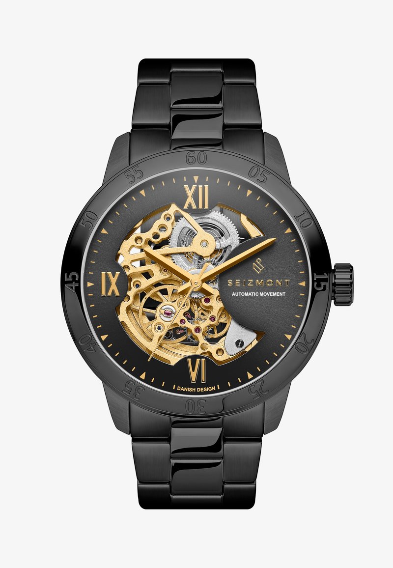 Automatisk klokke med svart metallarmbånd og -hus, gull- og sølvfarget mekanisk bevegelse synlig, svart urskive med gulldetaljer og markeringer.