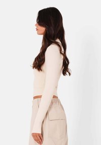 Creme kleurige top met lange mouwen en een nauwsluitend ontwerp, gecombineerd met hooggewaisted beige broeken met zijzakken. Soepele textuur en minimale details.