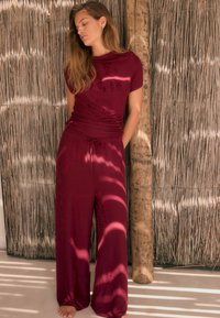 Burgundy dvoudílný outfit s přiléhavým topem a širokými kalhotami. Měkká tkanina s texturovaným vzorem a páskem na šňůrku.