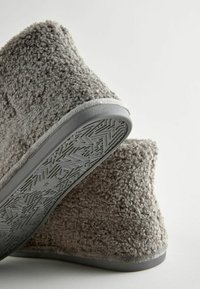 Graue, flauschige Hausschuhe zum Hineinschlüpfen mit einem strukturierten Stoff-Obermaterial und flexiblen Gummisohlen, die ein Zickzackmuster aufweisen.