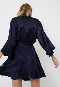 Robe en satin bleu marine de style kimono avec des manches évasées et un ourlet volant. Présente une ceinture en tissu assorti et une texture lisse et brillante.
