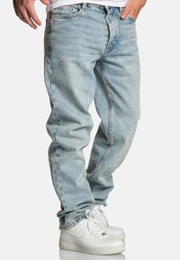 Jasnoniebieskie dżinsy o luźnym kroju, z pięcioma kieszeniami, suwakiem i subtelnym efektem sprania; zestawione z białymi sneakersami.