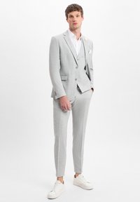 Light gray suit with textured fabric, slim-fit design, and notch lapels. Paired with a white shirt and white sneakers. Notable pocket square.