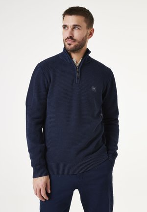 Suéter de punto azul marino con cuello con cremallera, diseño de punto texturizado, puños y dobladillo acanalados, que presenta un pequeño logo en el pecho.