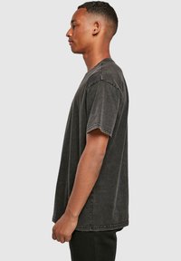 T-shirt noir surdimensionné avec un lavage vintage, présentant des manches courtes, un col rond et des coutures visible le long des coutures.