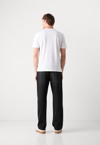 Hvid kortærmet t-shirt og sorte afslappede jeans med en glat tekstur og minimalistisk design. Footwear er hvide med en tan sål.