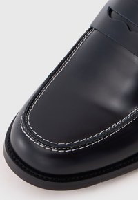 Dark blue leather loafers with white stitching, rounded toe, and a decorative strap across the top. Smooth texture with a polished finish.