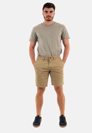 T-shirt grigio chiaro, pantaloni corti beige con chiusura a bottone e sneakers blu navy con dettagli arancioni. Outfit casual su una figura maschile.