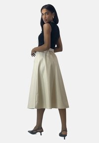 Zwarte geribde tanktop gecombineerd met een crèmekleurige rok tot op de knie, met een geplooide taille en een gladde textuur, afgewerkt met zwarte schoenen met hak.