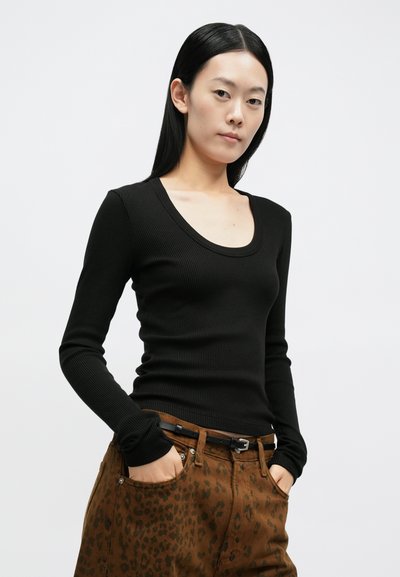 Top preto de manga comprida com nervuras e decote redondo, usado com calças castanhas com estampa de leopardo, com bolsos e um cinto preto.