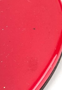 Gros plan d'une surface rouge brillante avec de légères éraflures, des taches et de petites taches noires et blanches sur le bord supérieur droit.