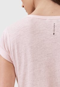 Top corto a maniche corte di colore rosa chiaro con una vestibilità rilassata. Presenta un colletto rotondo e un sottile logo del marchio stampato sulla parte posteriore. Tessuto morbido.
