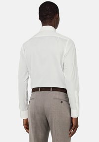 Camicia bianca a maniche lunghe con colletto classico, abbinata a pantaloni grigi chiari a quadri e una cintura marrone, mostrando una vista posteriore aerodinamica.