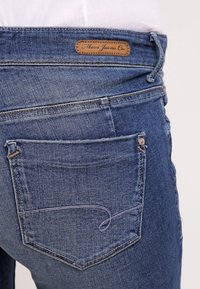 Jeans de mezclilla azul con una etiqueta de cuero de marca, que cuentan con un único bolsillo trasero con un sutil detalle de costura y un corte recto clásico.