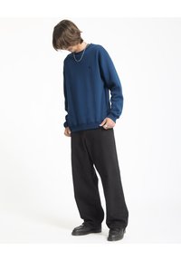 Marineblauwe sweatshirt met een ronde hals en geribbelde manchetten, gecombineerd met zwarte wijde broek en zwarte schoenen, met een subtiele logodetail.