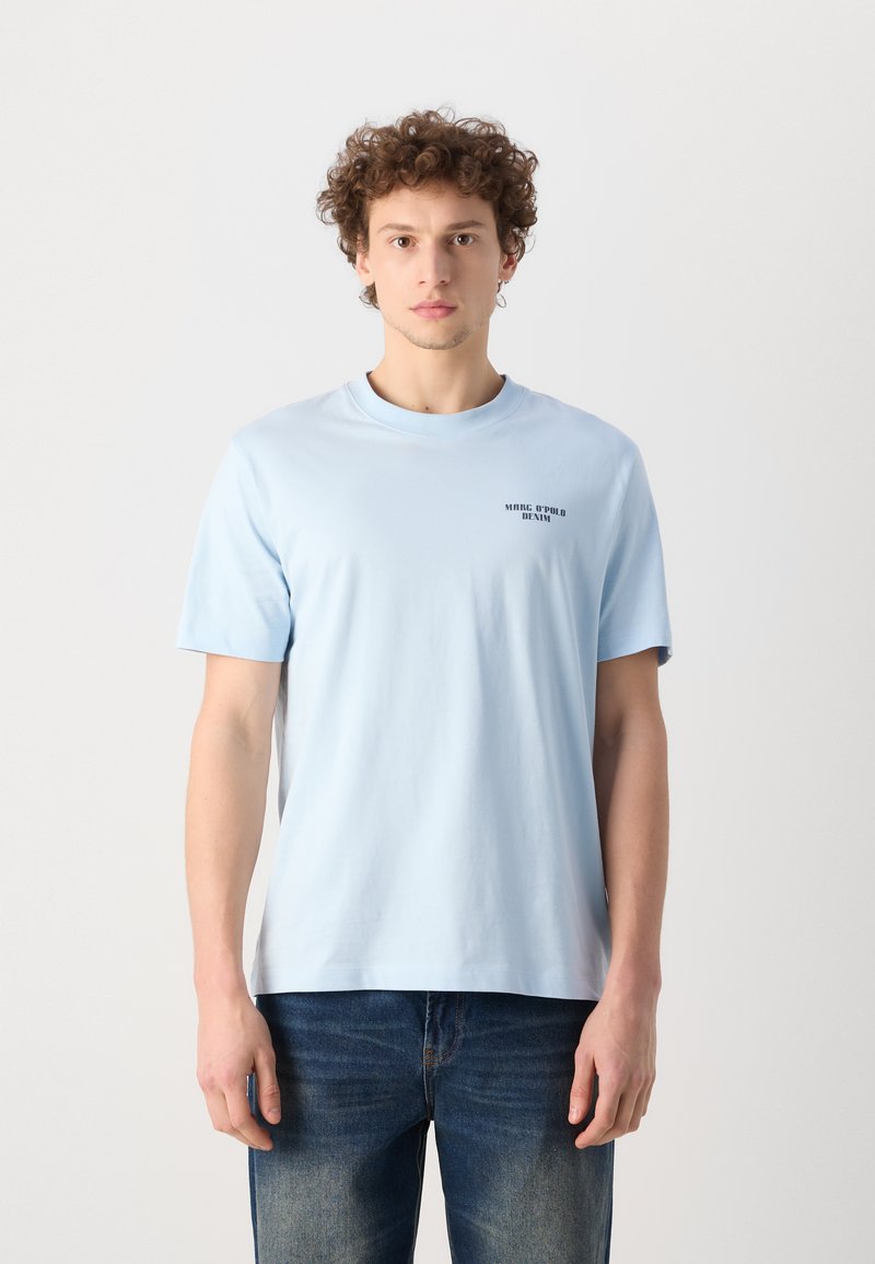 Hellblauses Baumwoll-T-Shirt mit kurzen Ärmeln, Rundhalsausschnitt und schwarzem Drucktext auf der oberen linken Seite. Getragen mit blauen Jeans.