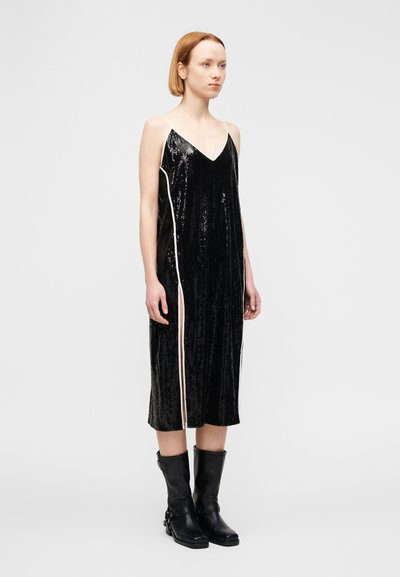Μαύρο αμάνικο φόρεμα με V-λαιμόκοψη, διακοσμημένο με κάθετες γυαλιστερές παγιέτες και λευκές πλαϊνές λεπτομέρειες. Συνδυάζεται με μαύρες μπότες μέχρι το γόνατο.
