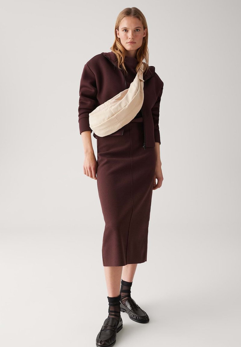 Gonna aderente bordeaux e felpa con cappuccio abbinati a una borsa a tracolla beige. Scarpe nere con dettagli testurizzati e calzini neri trasparenti. Stile semplice e moderno.