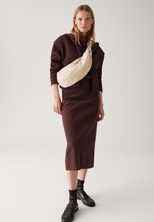 Maroon fitted skirt and hoodie with a beige crossbody bag. Black shoes with textured accents and sheer black socks. Simple, modern style.