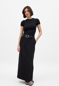 Zwarte aansluitende t-shirt gecombineerd met een hooggetailleerde maxi rok, geaccentueerd met een brede zwarte riem en gestreepte platte schoenen. Gladde stofstructuur.