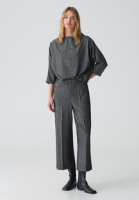 Grijze top met checkpatroon in oversized stijl en wijde mouwen, gecombineerd met bijpassende high-waisted broek. Beide gemaakt van textuurstof. Zwarte enkellaarsjes.
