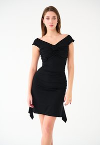 Czarna, dopasowana sukienka z dekoltem off-shoulder, marszczeniem w okolicy biustu i kwiatowym akcentem. Posiada asymetryczny dół.
