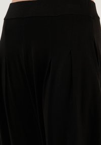 Zwarte broek met een soepele textuur, elastische tailleband en voorplooien voor extra detail en vorm.
