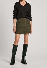 Black knit sweater with a v-neck, paired with a green plaid mini skirt and knee-high black heeled boots. Smooth texture and fitted design.