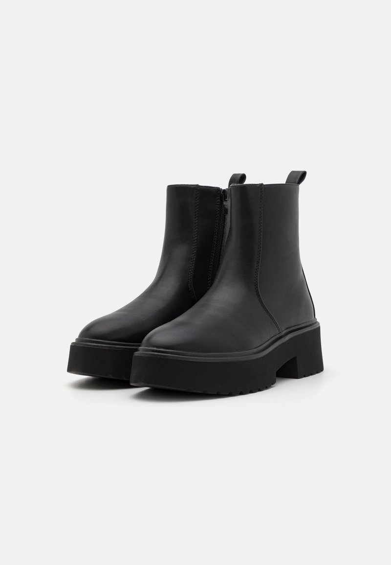 Botas de cuero negro hasta el tobillo con una suela de plataforma gruesa, cremallera lateral y lengüeta, que presentan una textura suave y un diseño minimalista.
