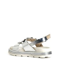 Sandali metallici argento con suola spessa, dotati di cinturini incrociati, accenti circolari e una cinghia posteriore alla caviglia per supporto.
