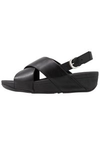 Svart lädersandal med korsade remmar, justerbar vristrem med silverfärgad spänne och kilklack.