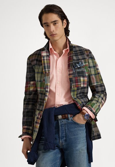 Kariran blazer iz večbarvnega blaga z kontrastno roza srajco, modro uro in mornarskim puloverjem, vse skupaj povezan okoli pasu, v kombinaciji z jeans hlačami.