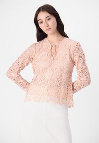 Pfirsichfarbene Spitzebluse mit langen Ärmeln und V-Ausschnitt; filigrane Blumendekore; Bindebanddetails vorne; gewellter Saum.