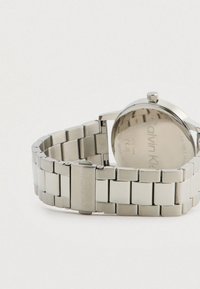 Montre-bracelet en métal argenté Calvin Klein avec bracelet à maillons, boucle déployante et logo gravé sur la boucle et à l'arrière de la montre.