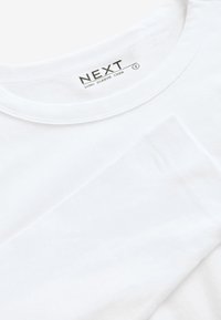 Chemise blanche à manches longues avec col rond et étiquette visible indiquant la taille small et la marque Next.