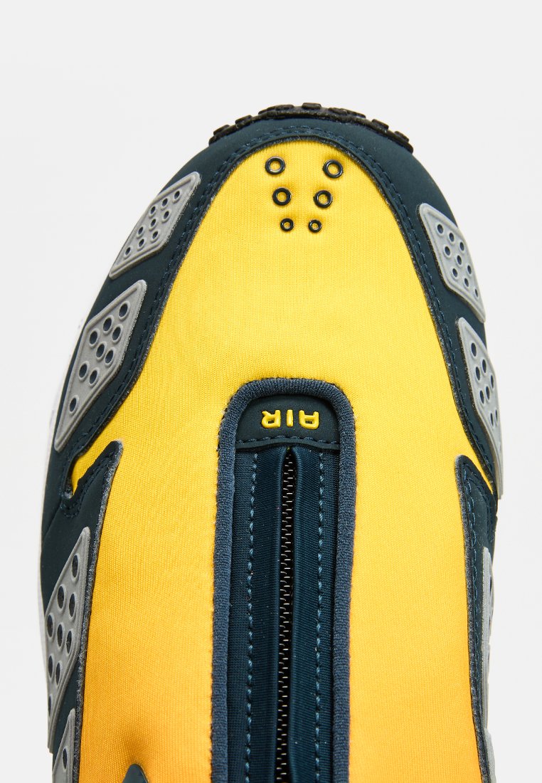Zapato de tela amarillo y azul marino con cierre de cremallera, acentos grises, agujeros de ventilación circulares y una suela texturizada para mayor agarre.