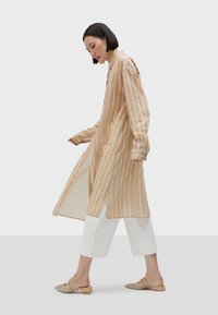 Beige randig lång skjorta med en avslappnad passform, med en knäppning framtill och uppvikta ärmar, ihopparad med vita capribyxor och beigea slip-on skor.