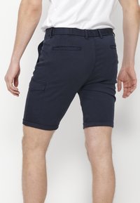 Shorts bleu marine en tissu léger, avec une coupe ajustée, poches sur les côtés et ourlets roulés. La vue de dos montre les détails de la taille.