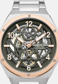 Automatyczny zegarek Kenneth Cole z bransoletą ze stali nierdzewnej, zieloną tarczą ukazującą wewnętrzne mechanizmy, różowo-złotymi akcentami oraz białymi znacznikami godzin.