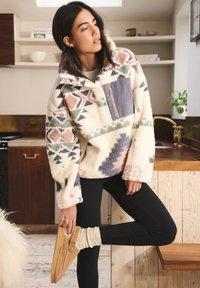 Pullover in pile con motivi geometrici in crema, rosa, verde e blu navy. Presenta una tasca con cerniera frontale e polsini a coste, abbinato a leggings neri.