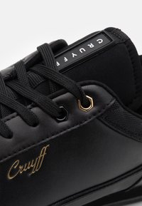 Schwarze Sneakers mit glattem synthetischen Obermaterial, runden schwarzen Schnürsenkeln und goldenen Akzenten auf dem Logo. Enthält sechseckige Ösen für die Schnürung.