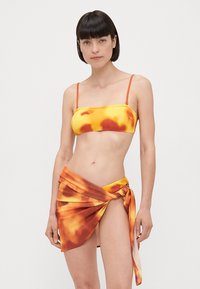 Top bikini giallo e arancione con motivo tie-dye, texture a coste e spalline sottili, abbinato a una gonna avvolgente coordinata con dettaglio a nodo.
