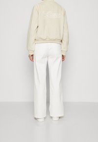 Pull crème avec "Guess" brodé dans le dos, associé à un jean blanc à jambes larges. Texture lisse avec poignets et ceinture côtelés.