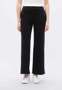 Μαύρο παντελόνι με φαρδιά γραμμή, μαλακή υφή και ελαστική ζώνη μέσης Calvin Klein, συνδυασμένο με λευκά αθλητικά παπούτσια. Εφαρμόζει στη μέση και είναι φαρδύ στα πόδια.