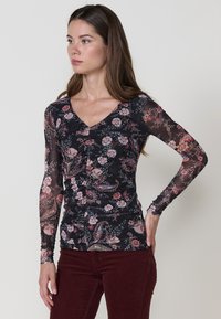 Top negro de manga larga con un diseño fruncido y escote en V. El material es transparente con patrones florales en rosa y crema. Combinado con pantalones color burdeos.