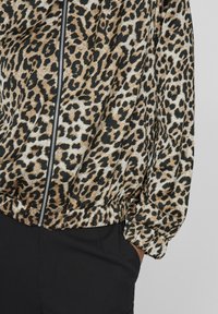 Giacca con stampa leopardata in tonalità di marrone e nero, caratterizzata da una chiusura con zip frontale, polsini elasticizzati e orlo arricciato per un look aderente.