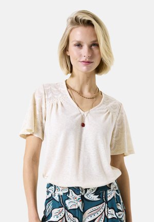 Crèmekleurig T-shirt met korte mouwen en kantdetails op de schouders, V-hals en een relaxte fit, gecombineerd met blauwe gemusterde broek.
