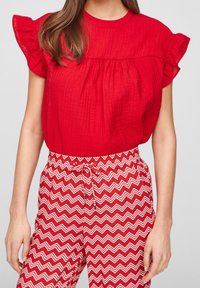 Blusa rossa con trama e maniche corte a volant, abbinata a pantaloni a zigzag rossi e bianchi con vita elasticizzata e cordoncino.
