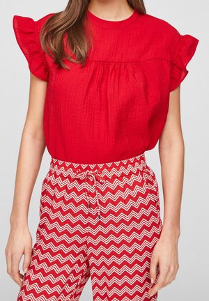 Blusa rossa con trama e maniche corte a volant, abbinata a pantaloni a zigzag rossi e bianchi con vita elasticizzata e cordoncino.